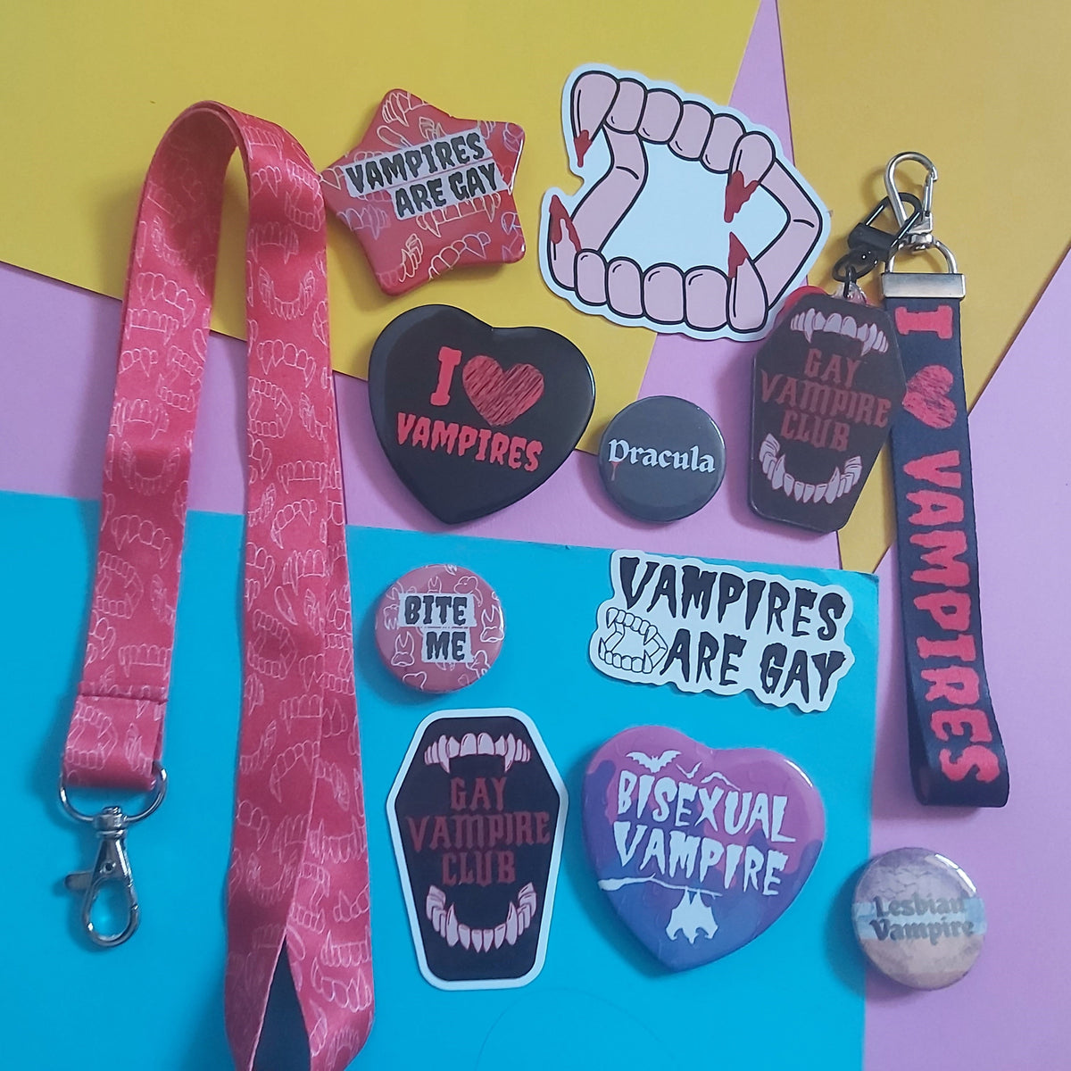 A pile of white die-cut stickers featuring the text 'VAMPIRES ARE GAY' in a black gothic font, accompanied by illustrations of vampire fangs, scattered over a background of matching stickers.