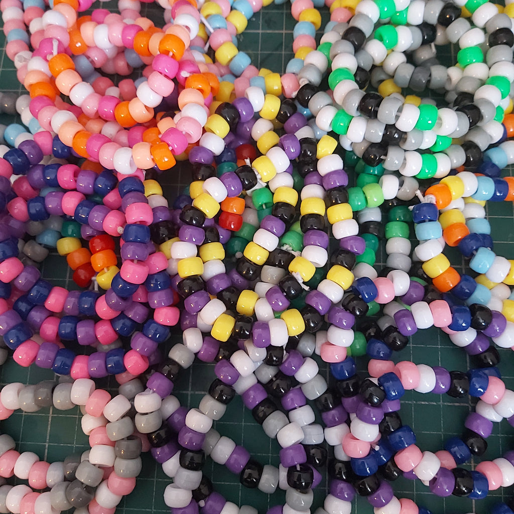 A large assortment of colourful beaded bracelets laid out on a green cutting mat. The beads come in many different colours, including pink, orange, yellow, purple, blue, green, black, and white, arranged in various patterns.