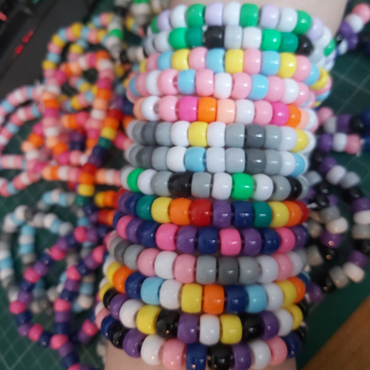 A stack of colorful beaded stretch bracelets worn on a wrist, featuring repeating patterns of various colors including pink, yellow, blue, green, orange, purple, and white.
