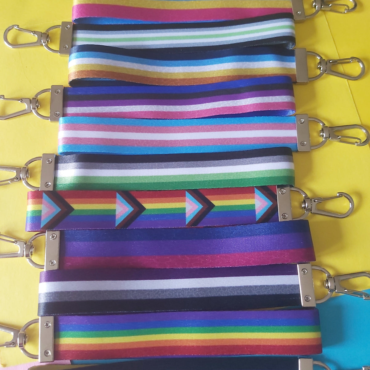 Colourful striped and patterned fabric straps with silver metal lobster clasps, arranged vertically on a bright yellow background.