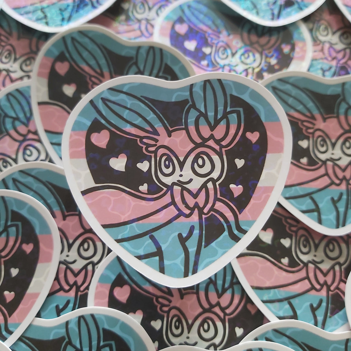 A close-up of multiple heart-shaped stickers featuring a stylized pokemoncharacter with pink, blue, and black colours, arranged overlapping on a yellow surface.