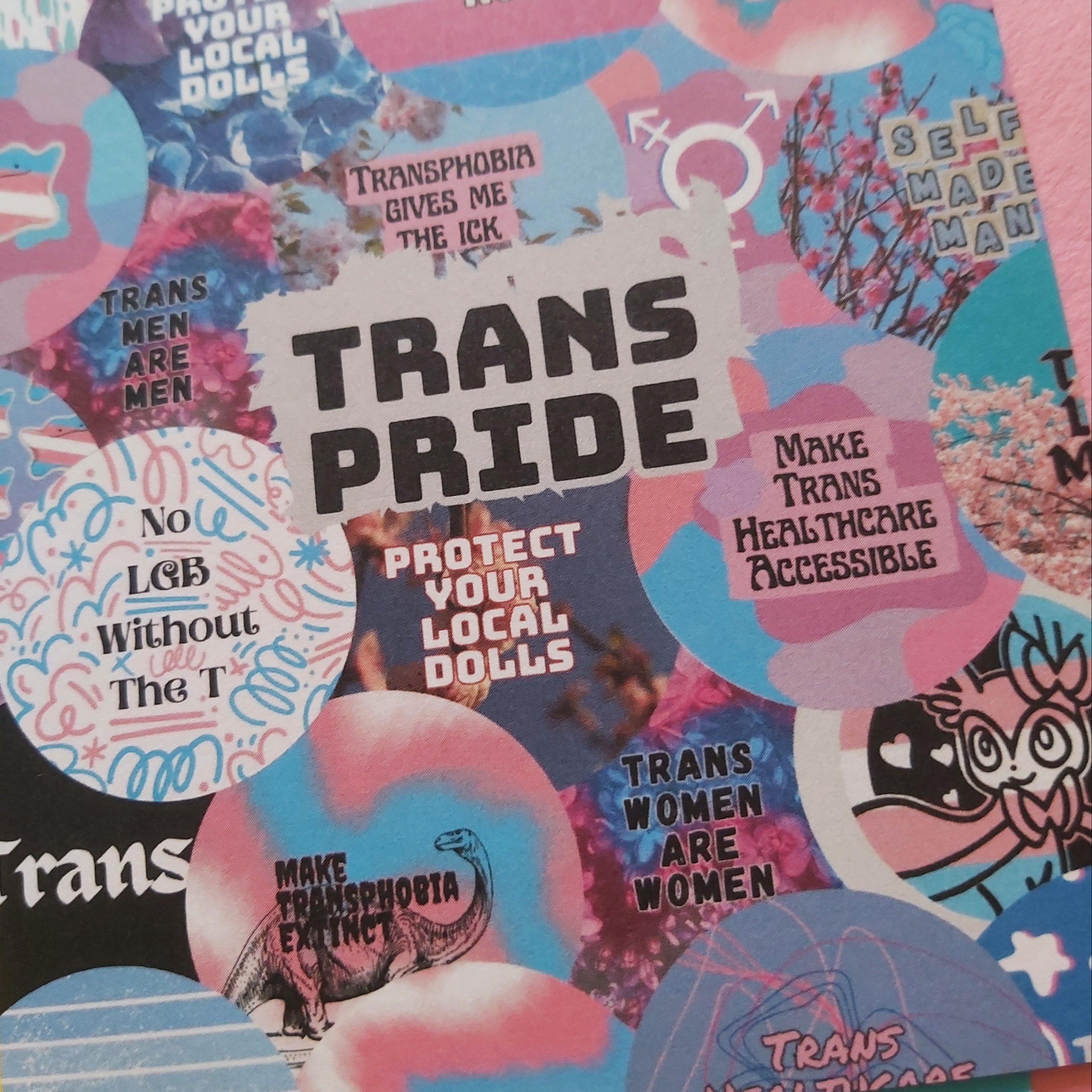 A print close-up featuring a vibrant collage of pink, blue, and white badges with various transgender rights slogans, illustrations, and symbols, with a bright yellow background visible at the bottom.