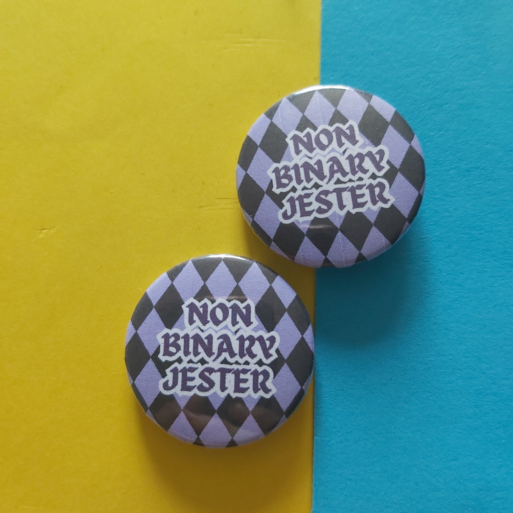 Two round pin-back buttons with a black and lavender argyle pattern and the text 'NON BINARY JESTER' in white, displayed on a split yellow and blue background.
