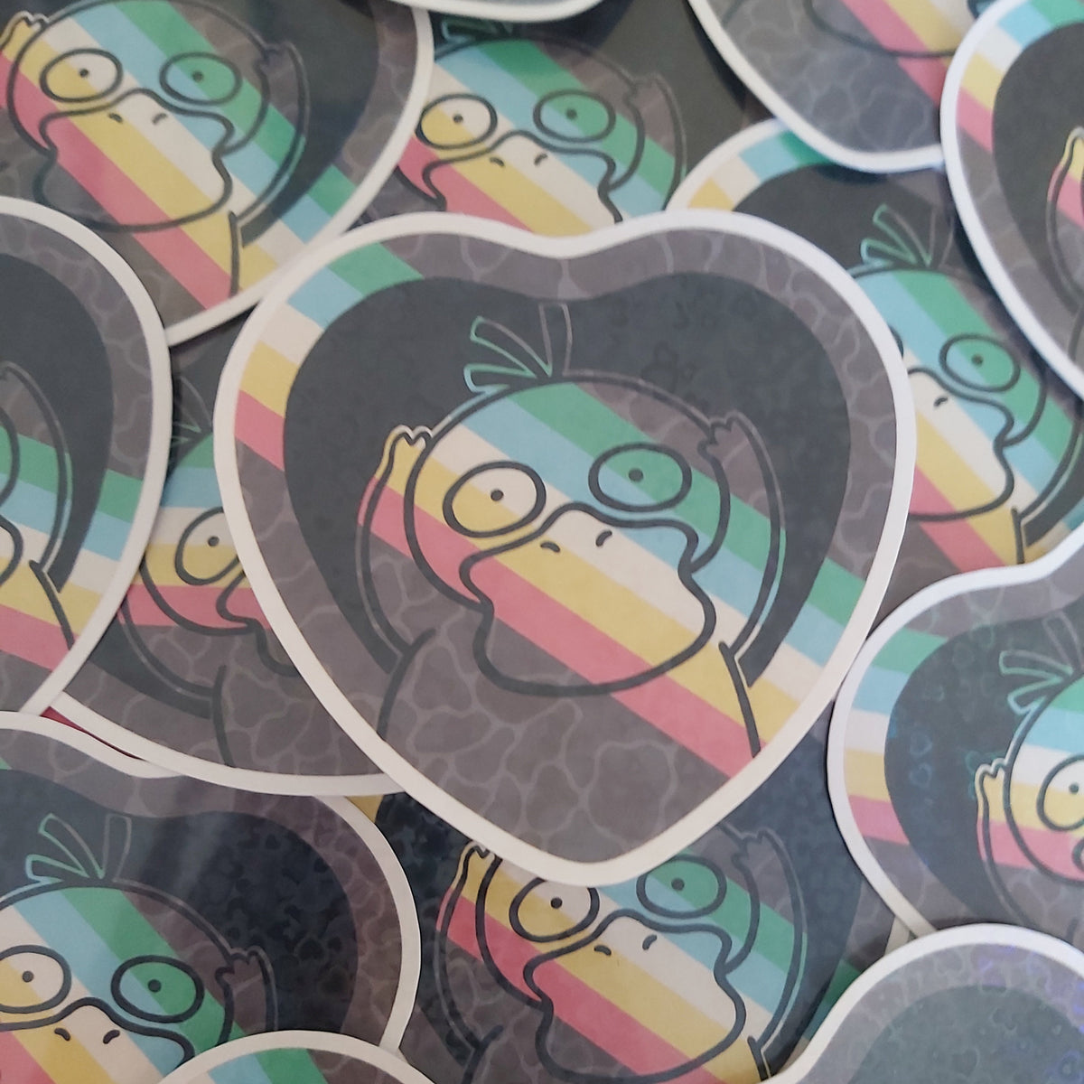 A pile of heart-shaped stickers featuring a cartoon pokemon character with rainbow stripes and a dark grey textured background.