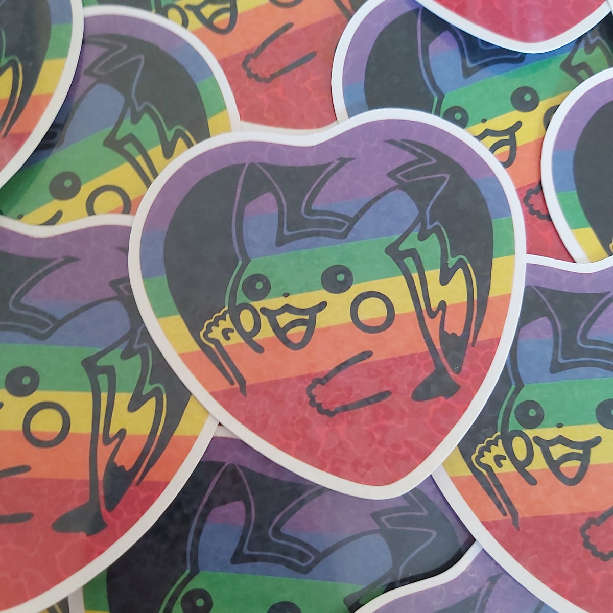 A close-up of overlapping heart-shaped stickers featuring a cartoon Pikachu with rainbow stripes and black line art, arranged on a white background.