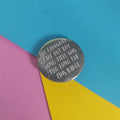 A round pin badge with white handwritten text reading 'MY FAVOURITE FALL OUT BOY SONG TITLE WAS TOO LONG FOR THIS BADGE', placed on a colorful background of cyan, pink, and yellow paper.