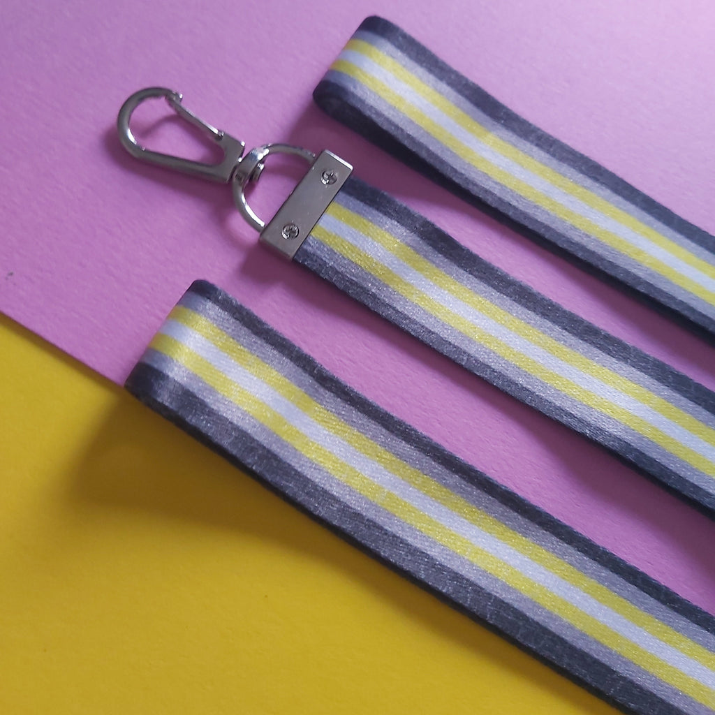 Three fabric strap accessories with a grey, white, and yellow striped pattern and silver metal clasp, laid flat on a split pink and yellow background.