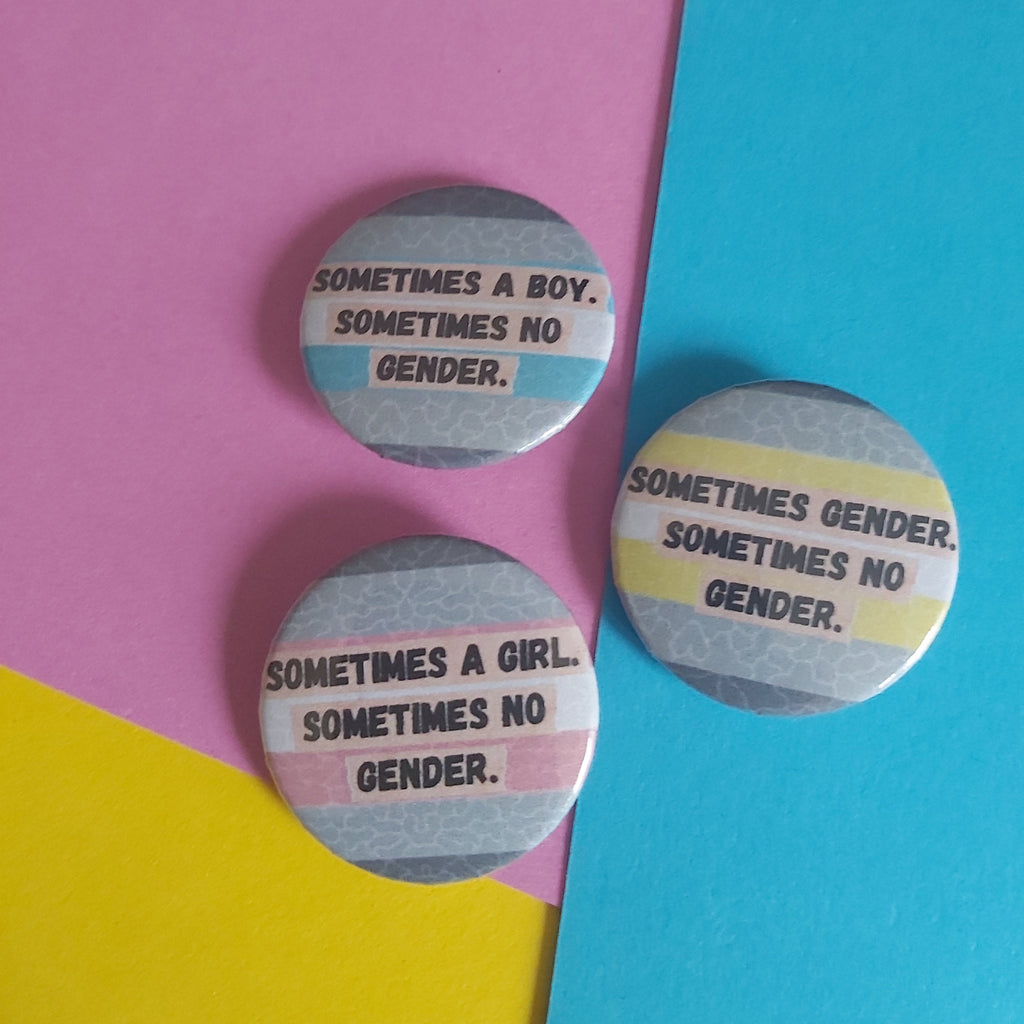 Three round pin-back buttons with the text 'SOMETIMES A GIRL. SOMETIMES NO GENDER, 'SOMETIMES A BOY. SOMETIMES NO GENDER or 'SOMETIMES GENDER. SOMETIMES NO GENDER