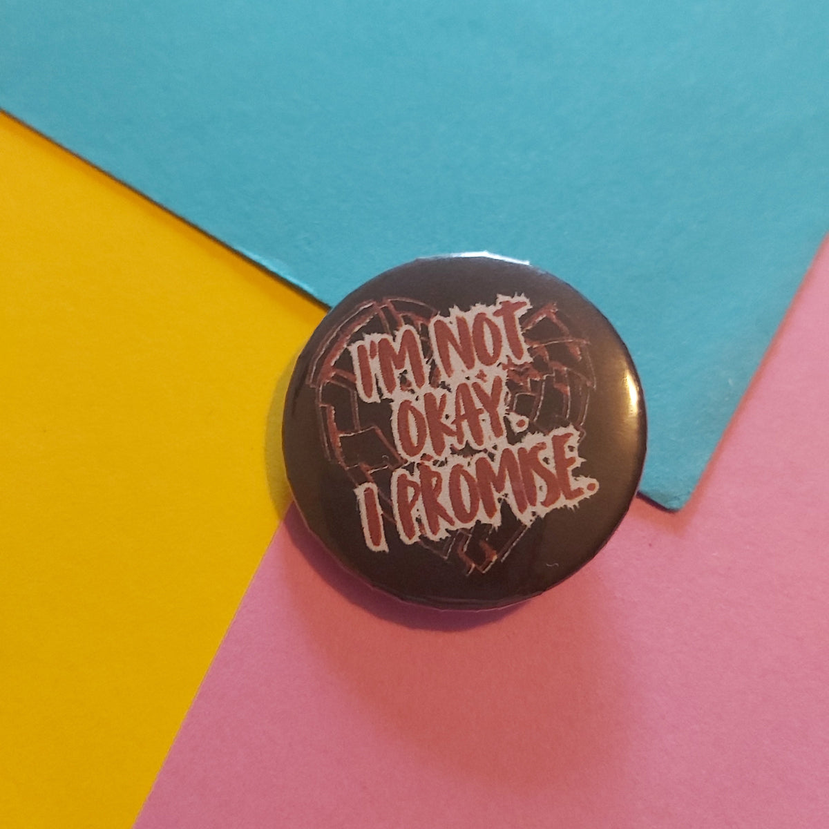 A round pin badge with the text 'I'M NOT OKAY. I PROMISE.