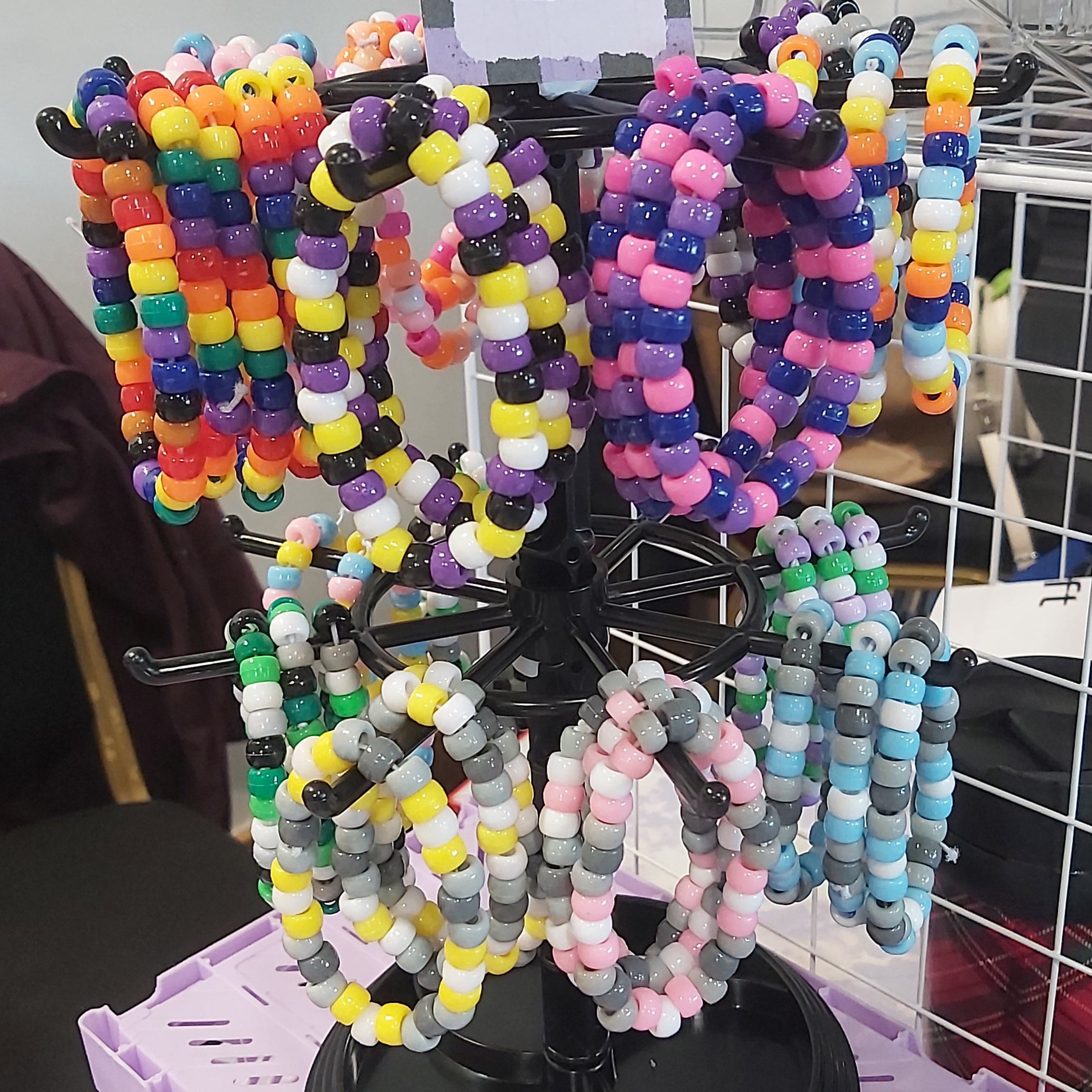 A black jewellery display stand filled with colourful beaded bracelets, including rainbow, pink, grey, and pastel varieties