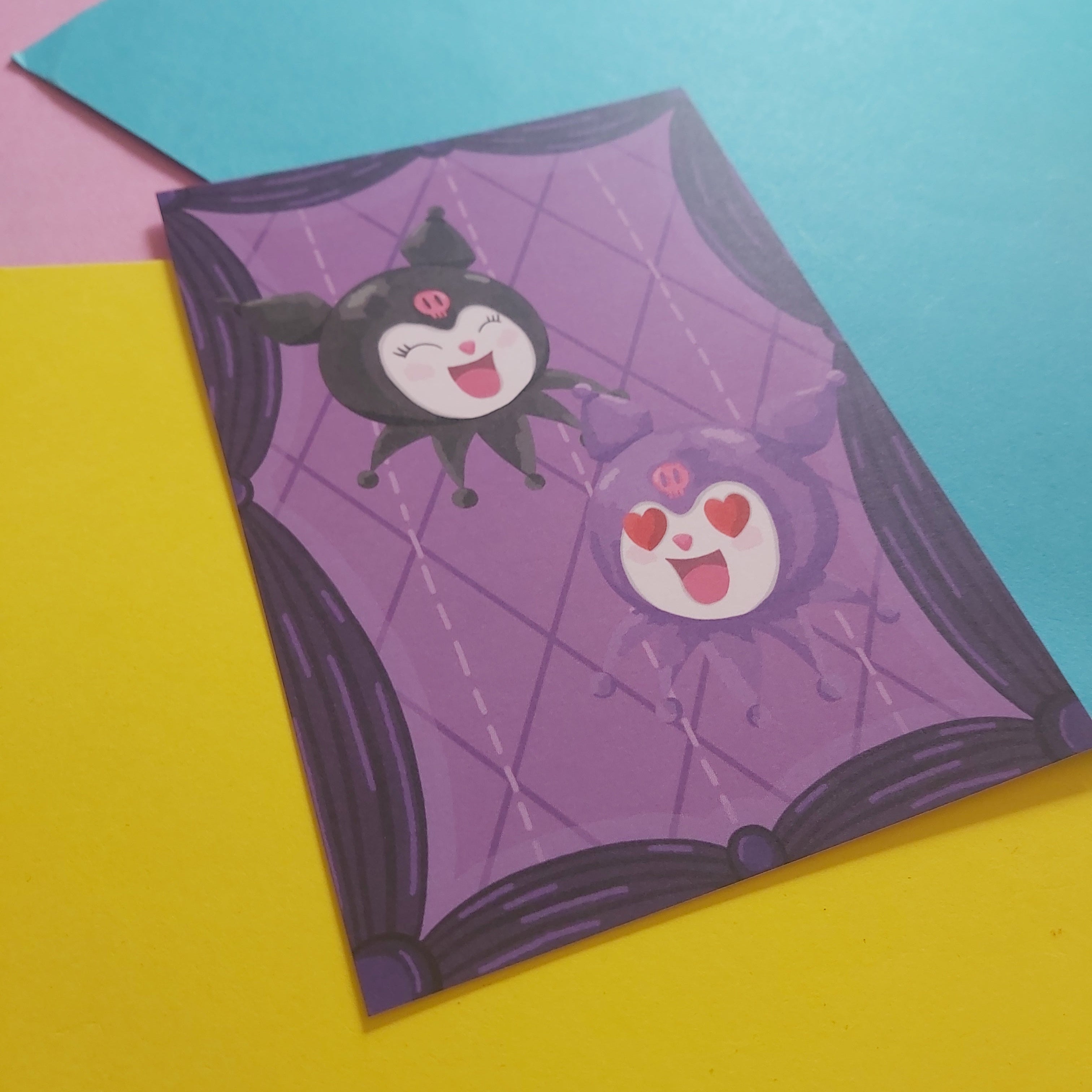 A print featuring two cute characters on a purple quilted background, photographed on a bright yellow surface with a blue sheet of paper behind it.