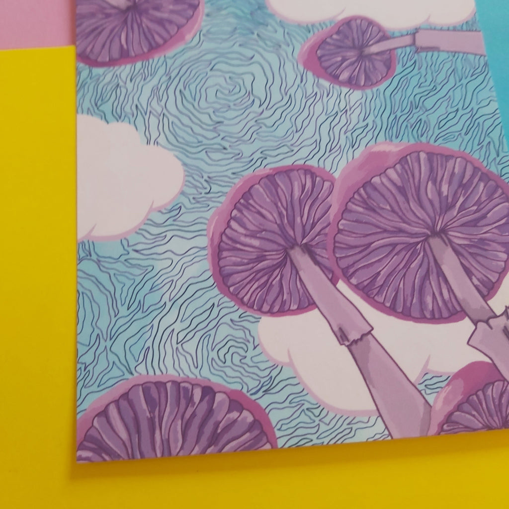 An art print featuring a psychedelic pattern of purple mushrooms and white clouds on a light blue background, styled on a colourful surface with yellow, pink, and blue paper visible around it.