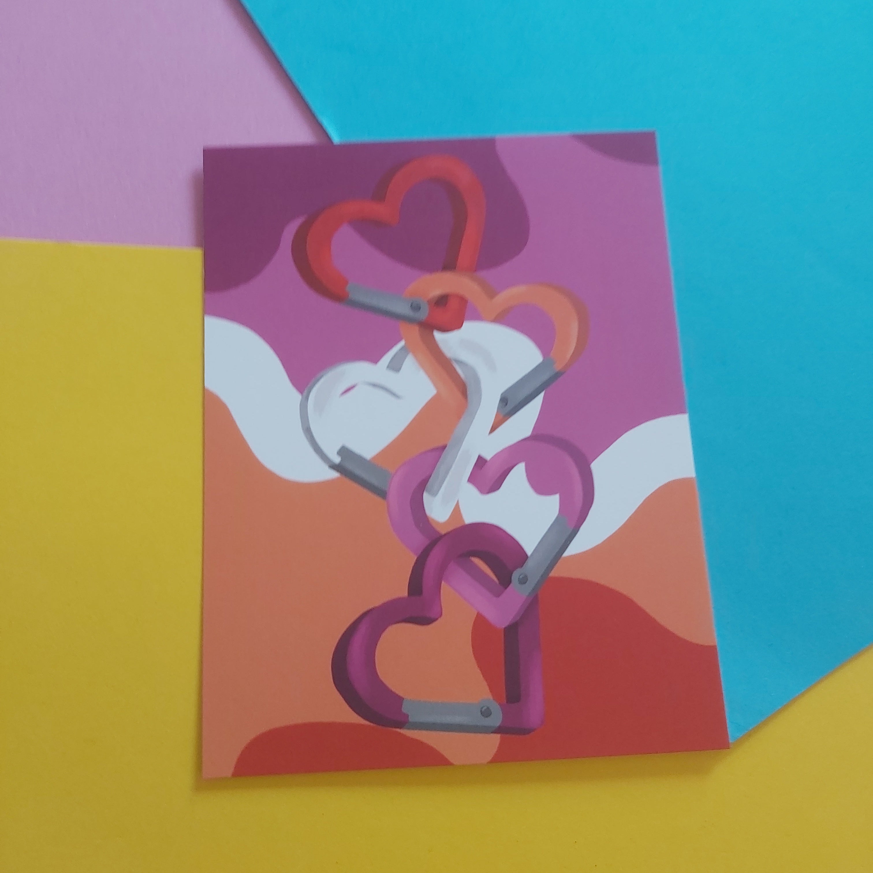 An art print featuring a stylised illustration of interlocking hearts in shades of pink, red, and orange, displayed on a colourful background of yellow, pink, and blue paper.