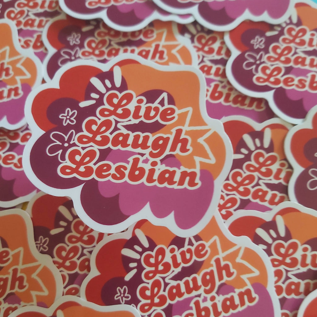 A pile of die-cut stickers featuring the phrase 'Live Laugh Lesbian' in red script over retro orange, pink, floral shapes with white outlines.