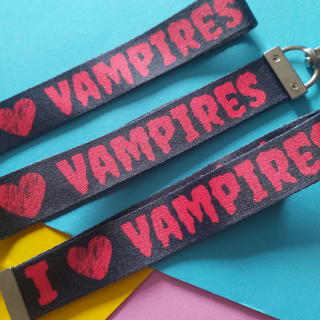 Three black fabric keychains with red text and heart designs, arranged diagonally on a colorful background of turquoise, yellow, and pink paper.