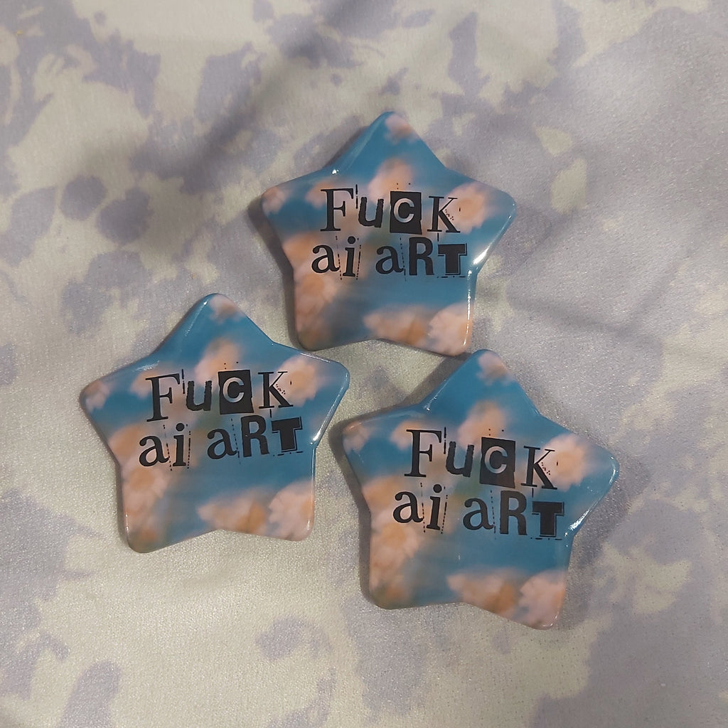 Three star-shaped pins with a blue and white tie-dye pattern, each printed with the text 'FUCK AI ART' in black, arranged on a light purple and white tie-dye fabric background.