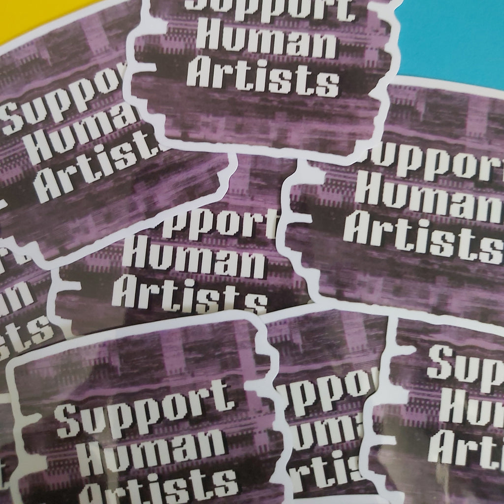 A pile of die-cut stickers with the text 'Support Human Artists' in white over a purple abstract background, photographed on a split yellow and blue surface.