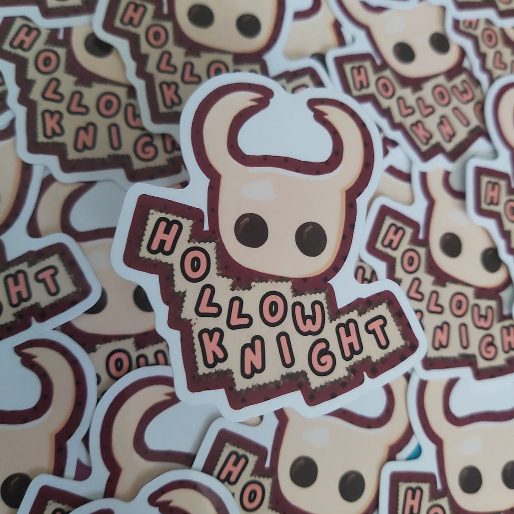 A pile of die-cut stickers featuring a cartoon horned knight head and the words 'HOLLOW KNIGHT' in a stylized font, photographed close up.