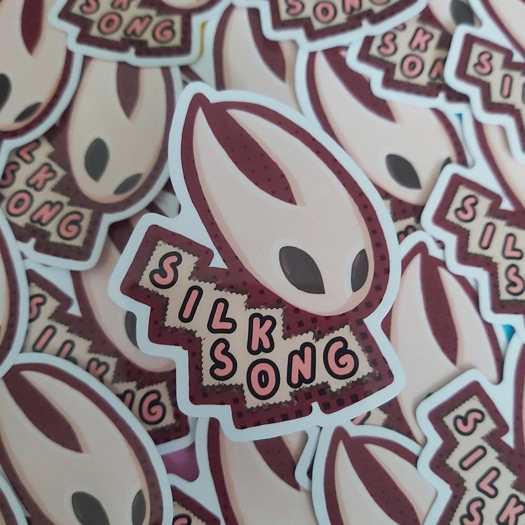 A pile of die-cut stickers featuring a stylized alien head with the text 'SILK SONG' on a maroon label, photographed close up.