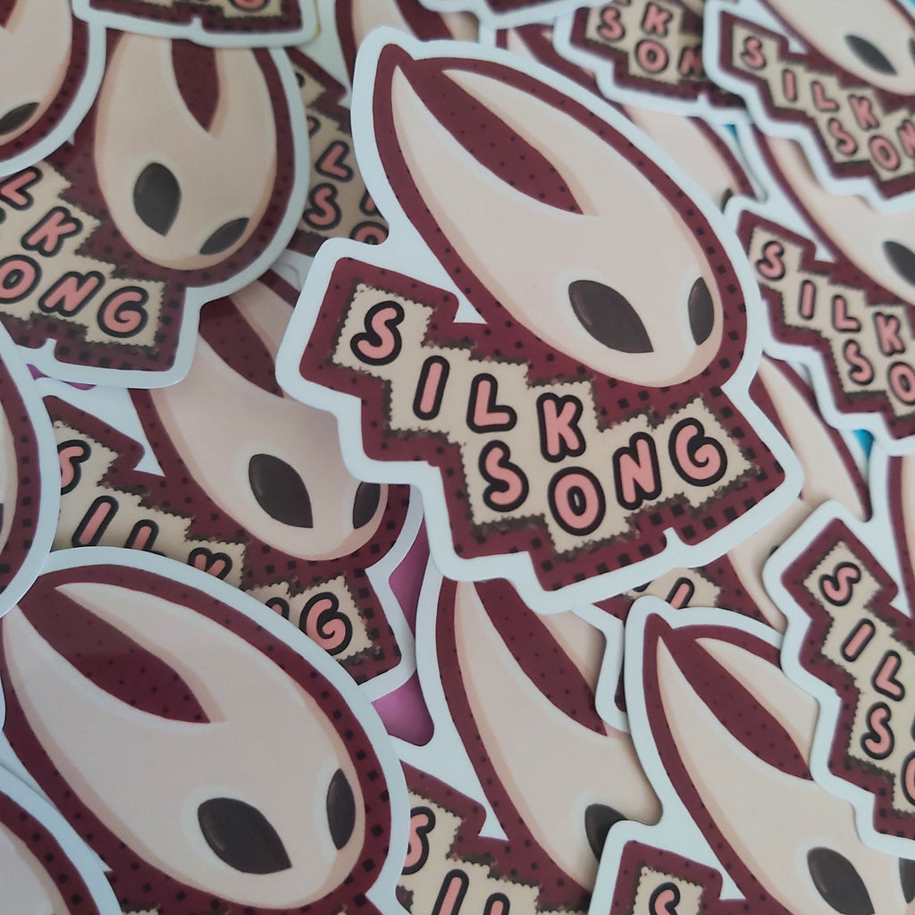 A close-up pile of die-cut stickers featuring a stylized alien head and the words 'SILK SONG' in pink lettering on a dark red banner.