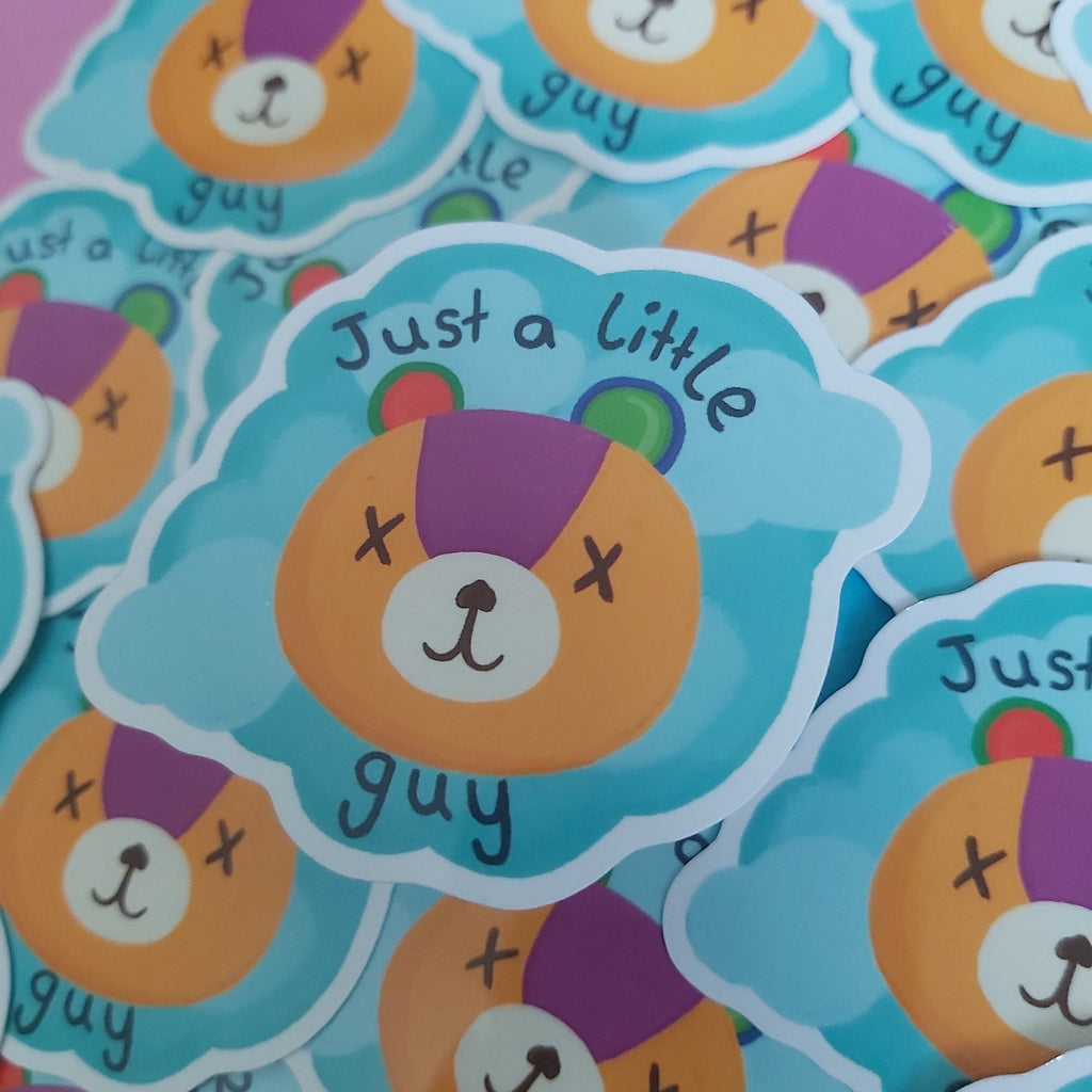 A close-up of multiple die-cut stickers featuring a cartoon bear face with the text 'Just a little guy' on a light blue cloud-shaped background.