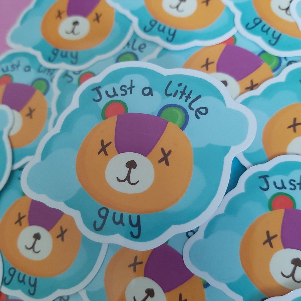 A close-up of multiple die-cut stickers featuring a cartoon bear face with the text 'Just a little guy' on a light blue cloud-shaped background.