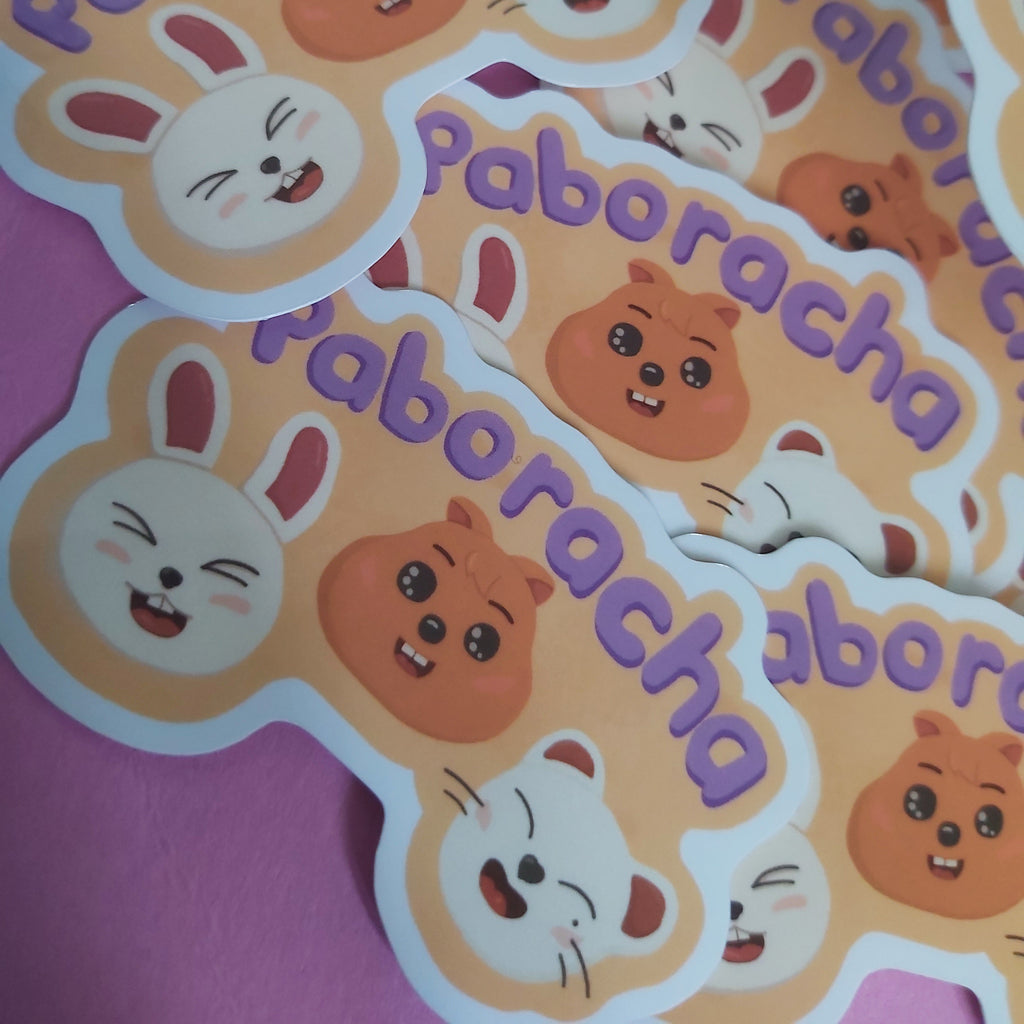 A pile of die-cut stickers featuring cute cartoon animal faces with the word 'Paboracha' in purple text, arranged on a pink surface.