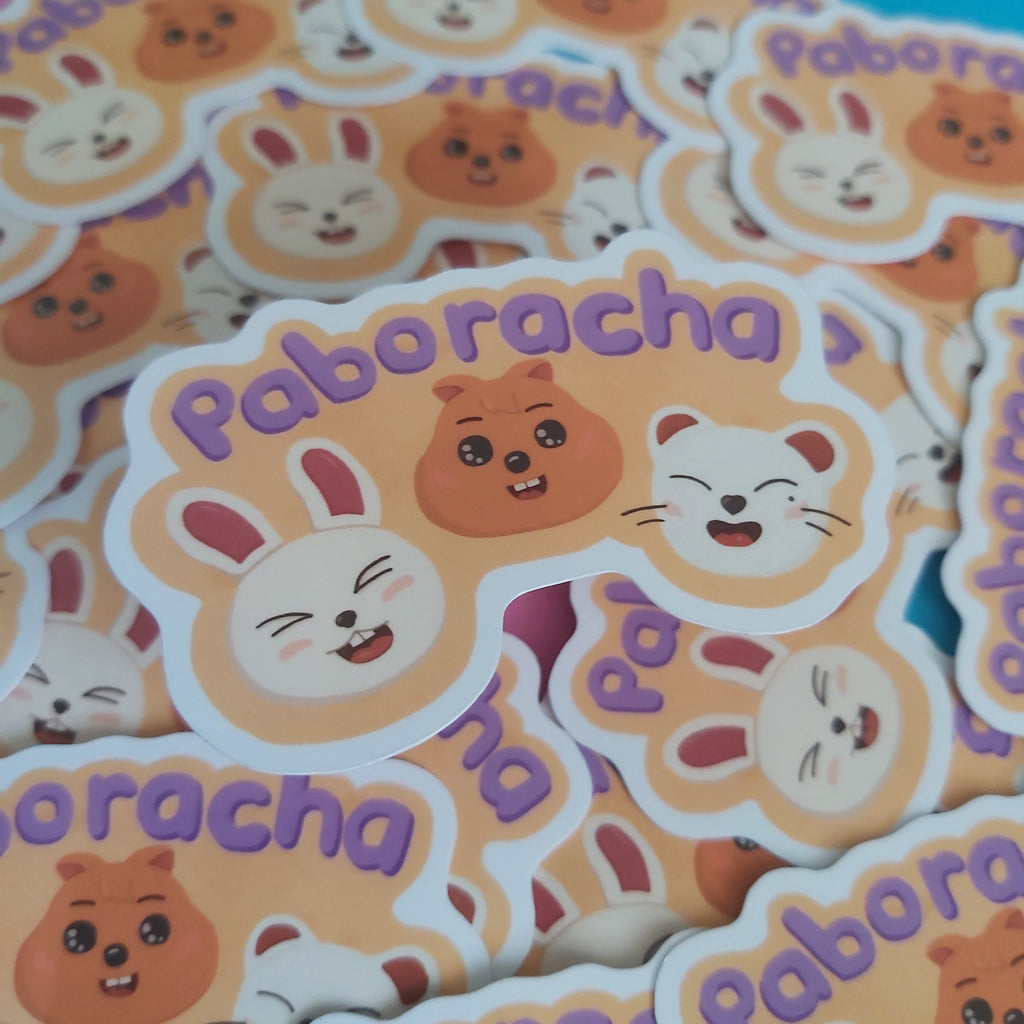 A pile of die-cut stickers featuring cute cartoon animal faces and the word 'Paboracha' in purple lettering, photographed close up on a colorful background.