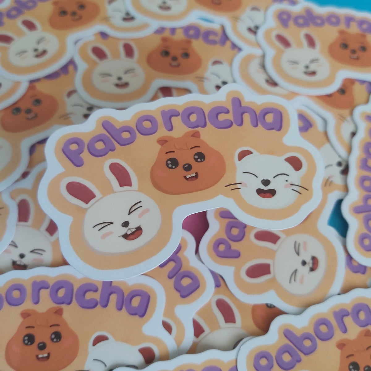 A pile of die-cut stickers featuring cute cartoon animal faces and the word 'Paboracha' in purple lettering, photographed close up on a colorful background.