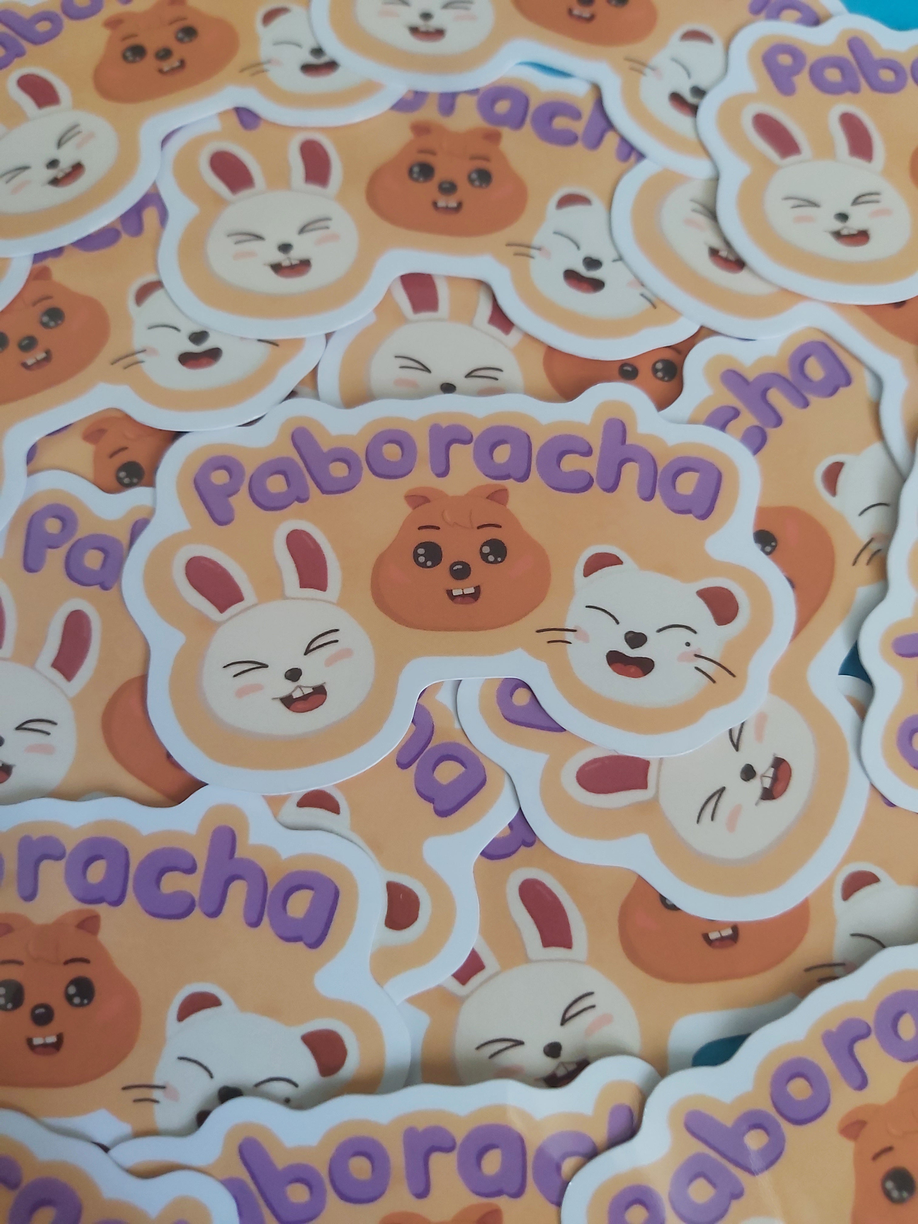 A pile of die-cut stickers featuring cute cartoon animal faces and the word 'paboracha' in purple text on a peach background.