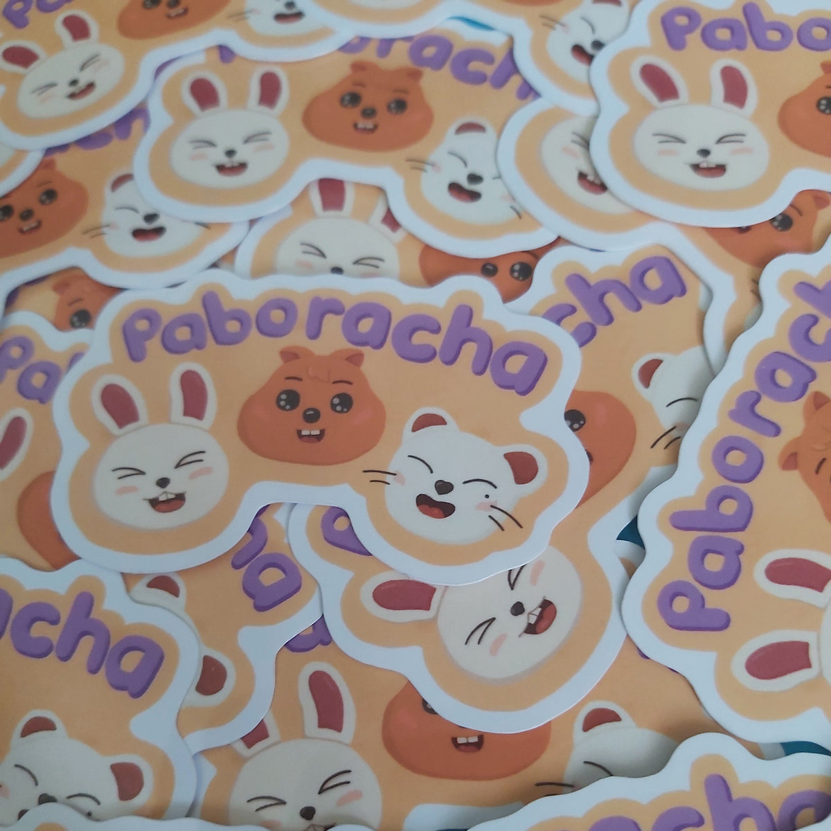 A pile of die-cut stickers featuring cartoon animal faces and the word 'Paboracha' in purple text on a peach background.