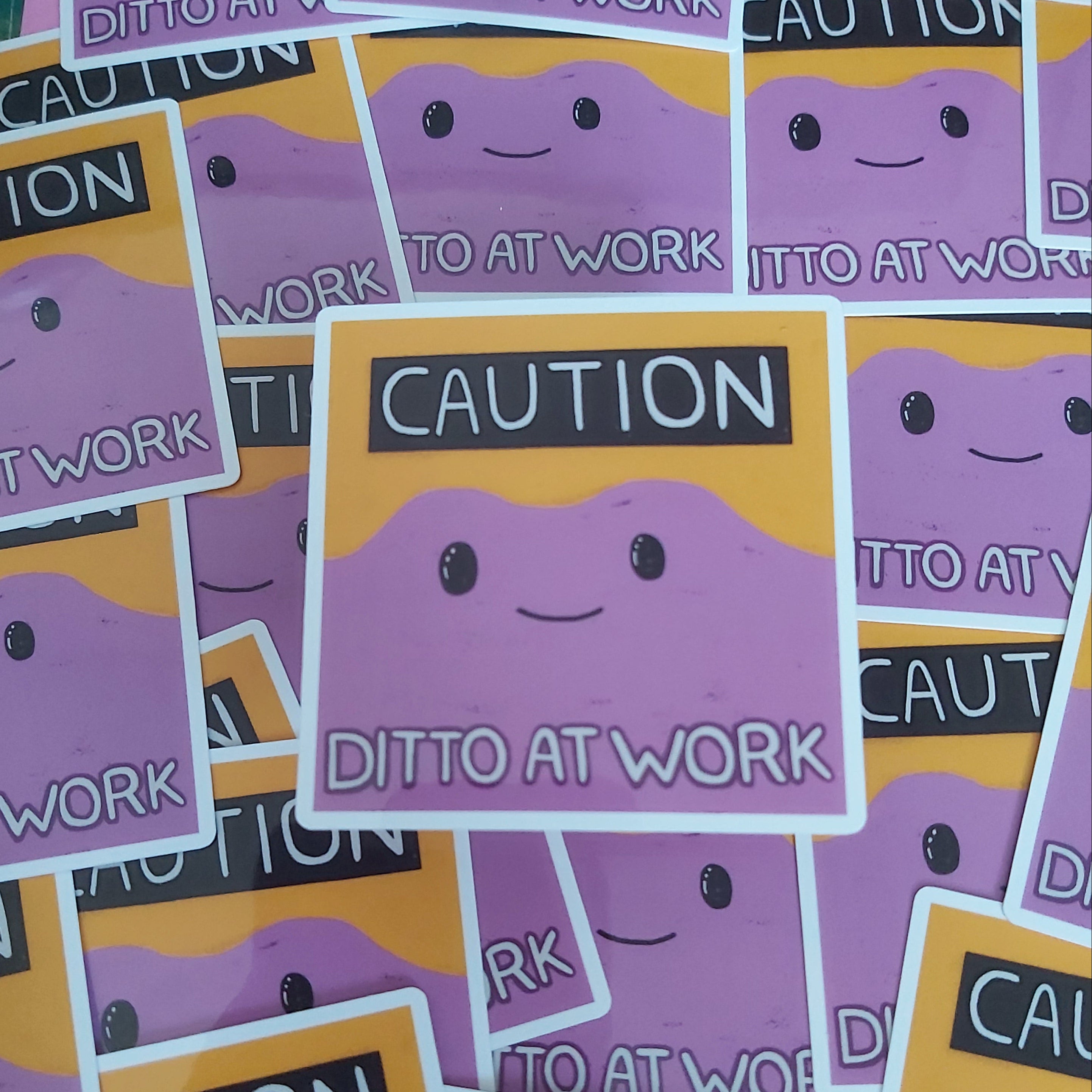 A pile of square stickers featuring a purple cartoon face with black eyes and a smile, set against a yellow background with the words 'CAUTION DITTO AT WORK' in white and black text.
