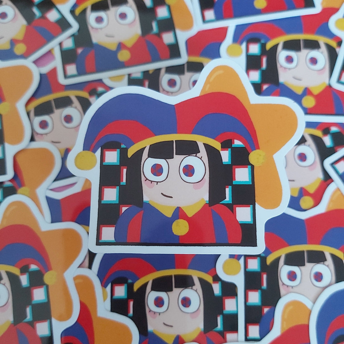 A close-up pile of colorful cartoon character stickers featuring a jester-like character with a blue, red, yellow, and black hat, repeated across the frame.