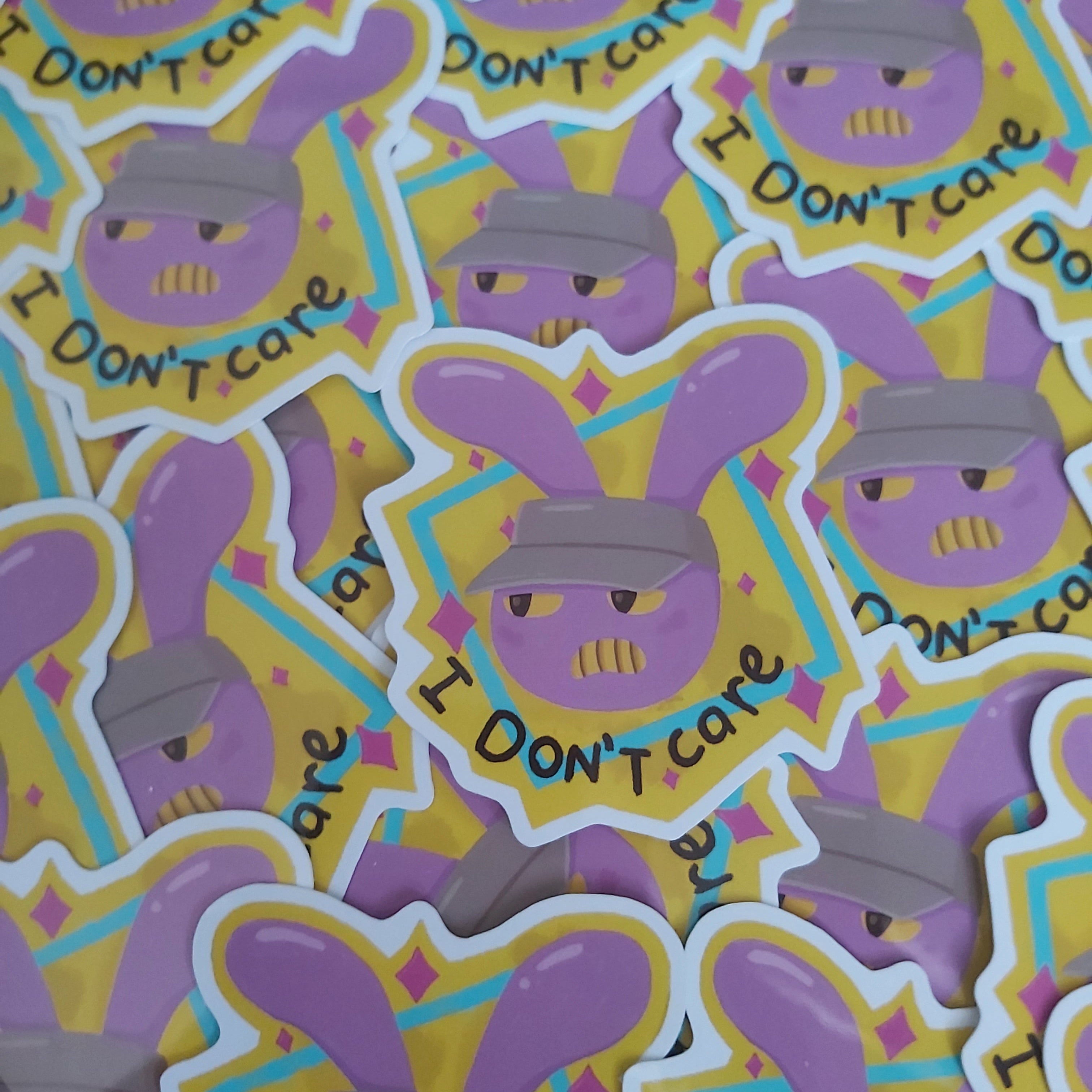 A pile of die-cut stickers featuring a cartoon bunny wearing a gray cap with the text 'I DON'T care' in yellow, set against a background of matching stickers.