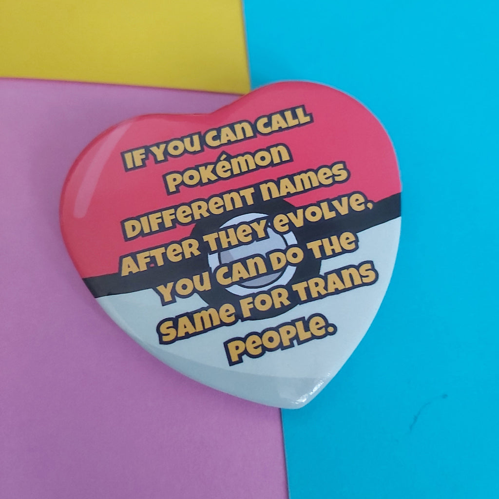A heart-shaped Pokémon-themed button pin with a red and white design and yellow text reading, 'IF YOU CAN CALL POKÉMON DIFFERENT NAMES AFTER THEY EVOLVE, YOU CAN DO THE SAME FOR TRANS PEOPLE,' shown on a colourful pastel background.