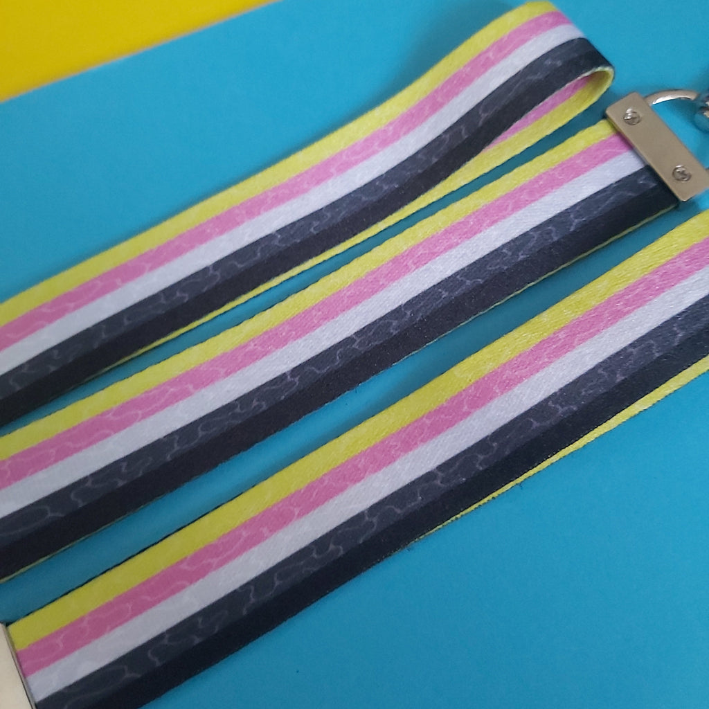 A close-up of a striped fabric lanyard with a metal lobster clasp, laid diagonally on a bright blue background with a yellow corner visible.