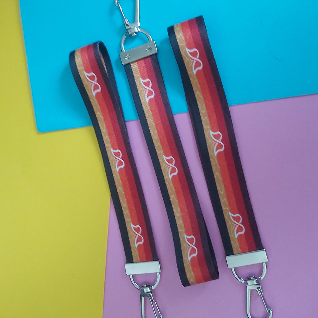 Three fabric keychains with red, orange, brown, and white butterfly motifs and silver metal clasps, displayed on a split yellow, blue, and pink background.