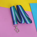 A gay male pride flag striped lanyard with a silver lobster clasp, laid flat on a colorful background of pink, yellow, and blue paper.