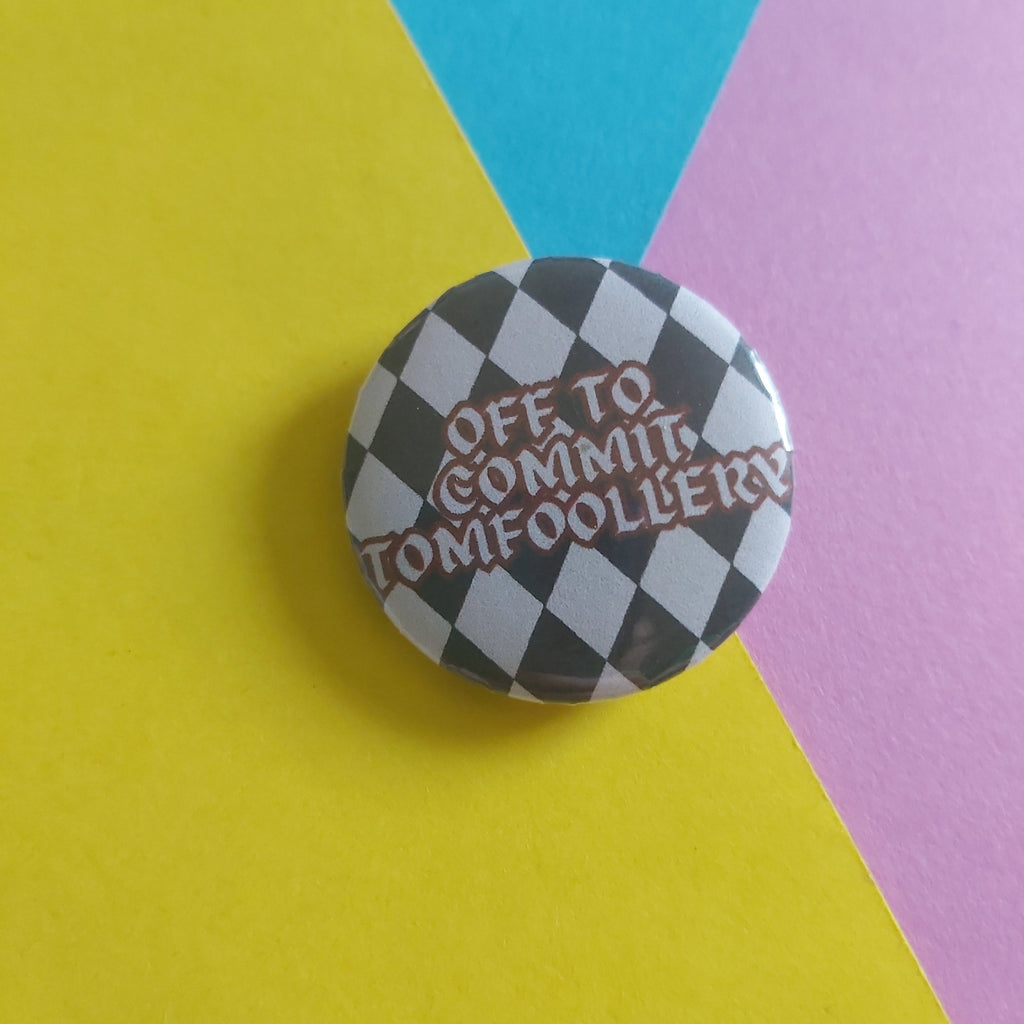 A round pinback button with a black and white checkered pattern and the text 'OFF TO COMMIT TOMFOOLERY' in red, placed on a diagonally split yellow, blue, and pink background.