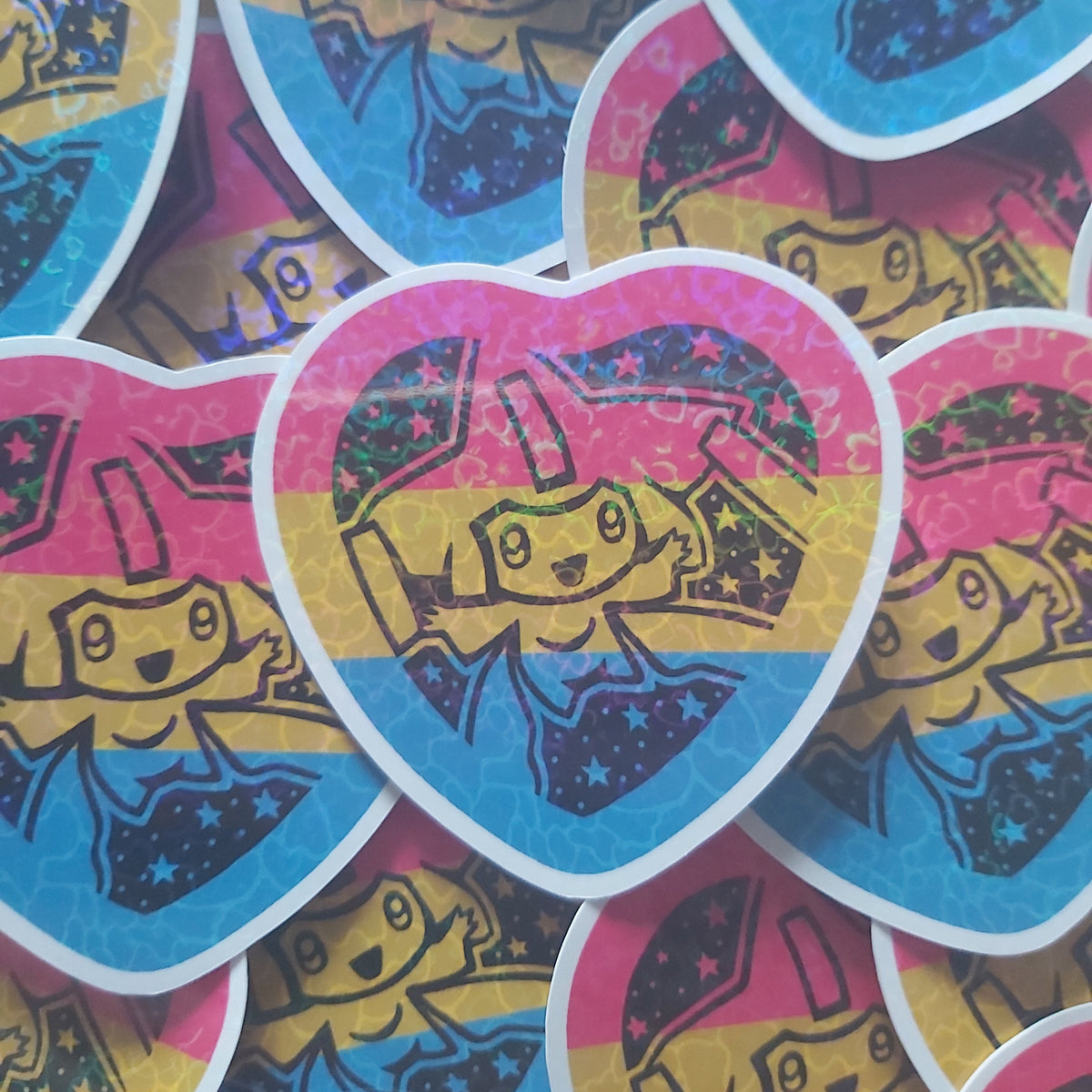 A close-up pile of heart-shaped stickers featuring a cartoon Pokémon design with pink, blue, and yellow colours.