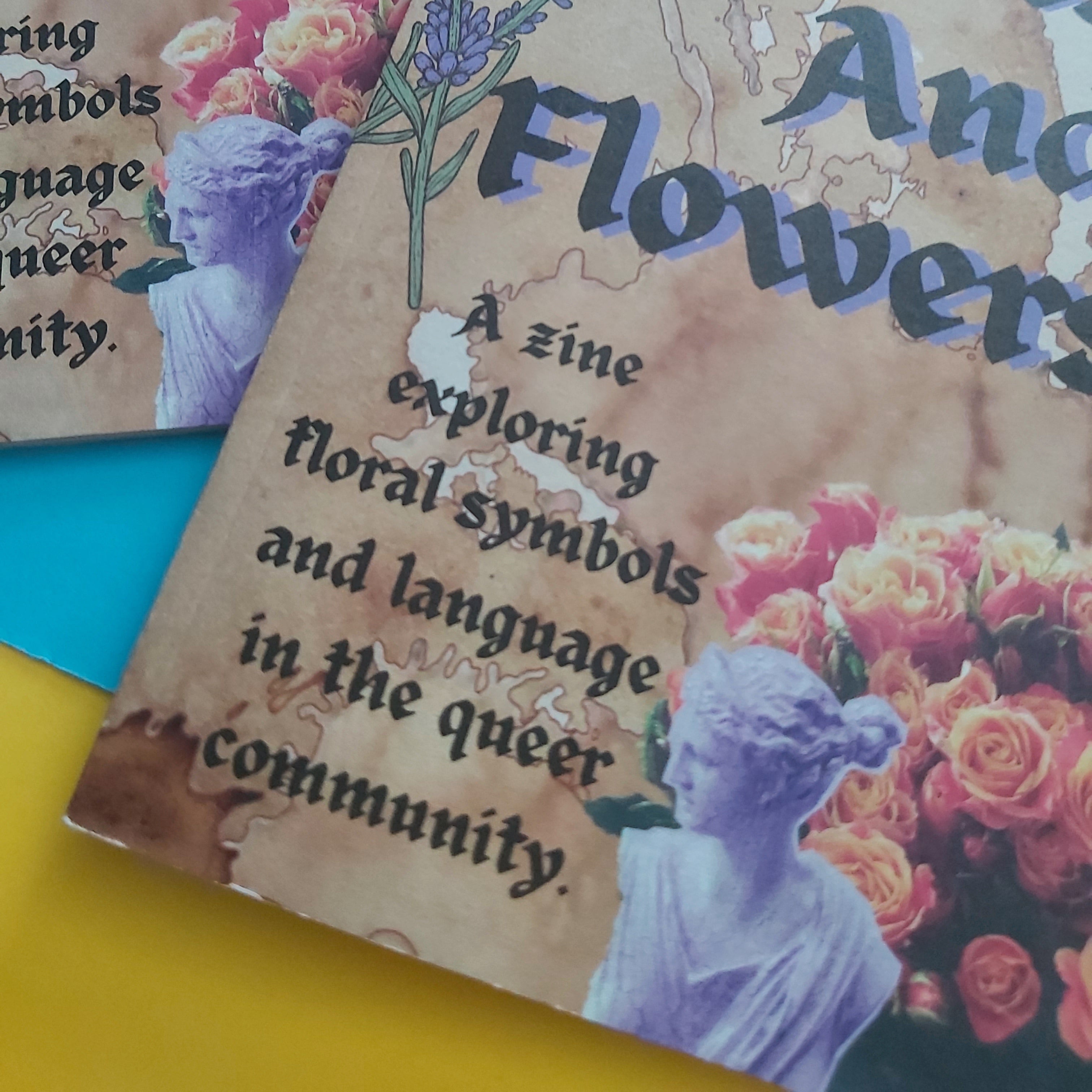 A close-up of a printed zine cover  featuring floral artwork, a statue illustration, and the text 'A zine exploring floral symbols and language in the queer community.' Another similar cover is partially visible behind it on a bright yellow surface.