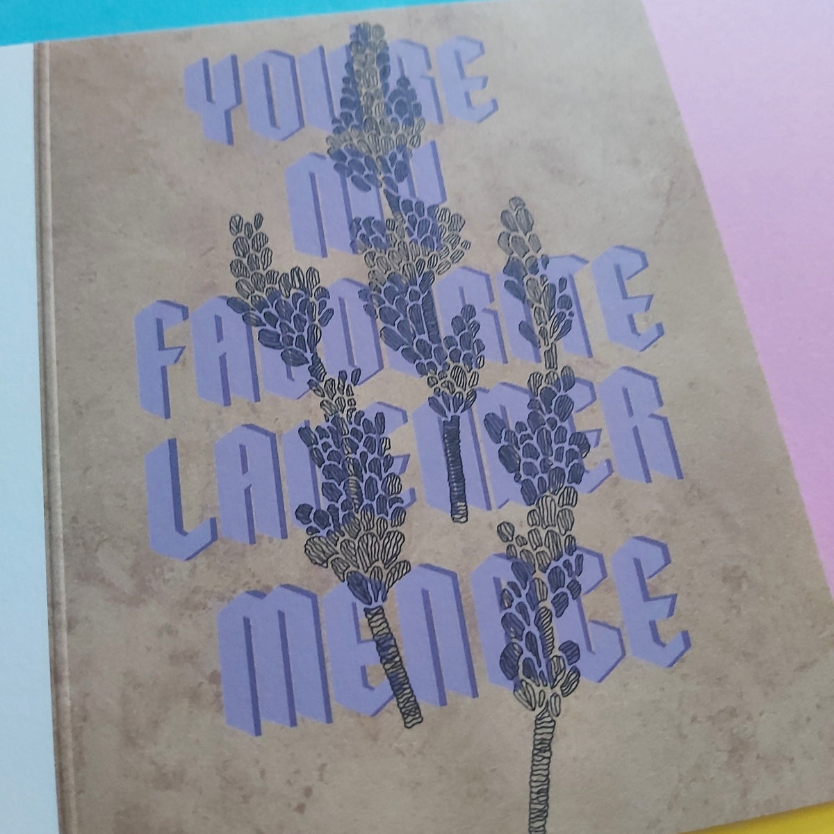 A greeting card with a textured beige background featuring the phrase 'YOU'RE MY FAVORITE LAVENDER MENCE' in lavender-purple lettering overlaid with illustrations of lavender sprigs.