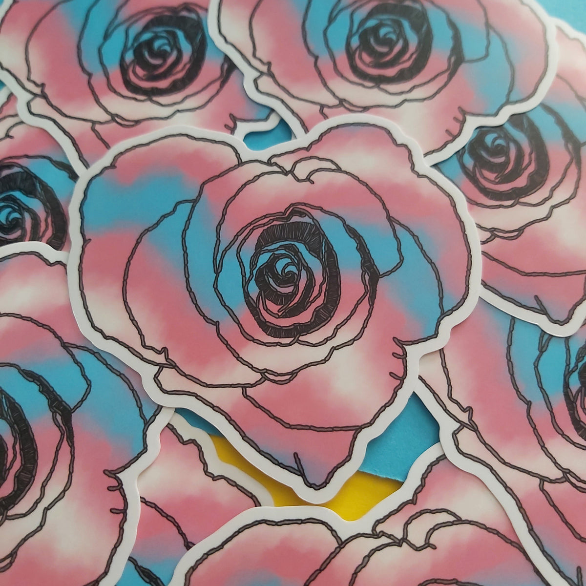A close-up of multiple die-cut stickers featuring stylised pink and blue roses with black outlines, arranged on a bright blue background.