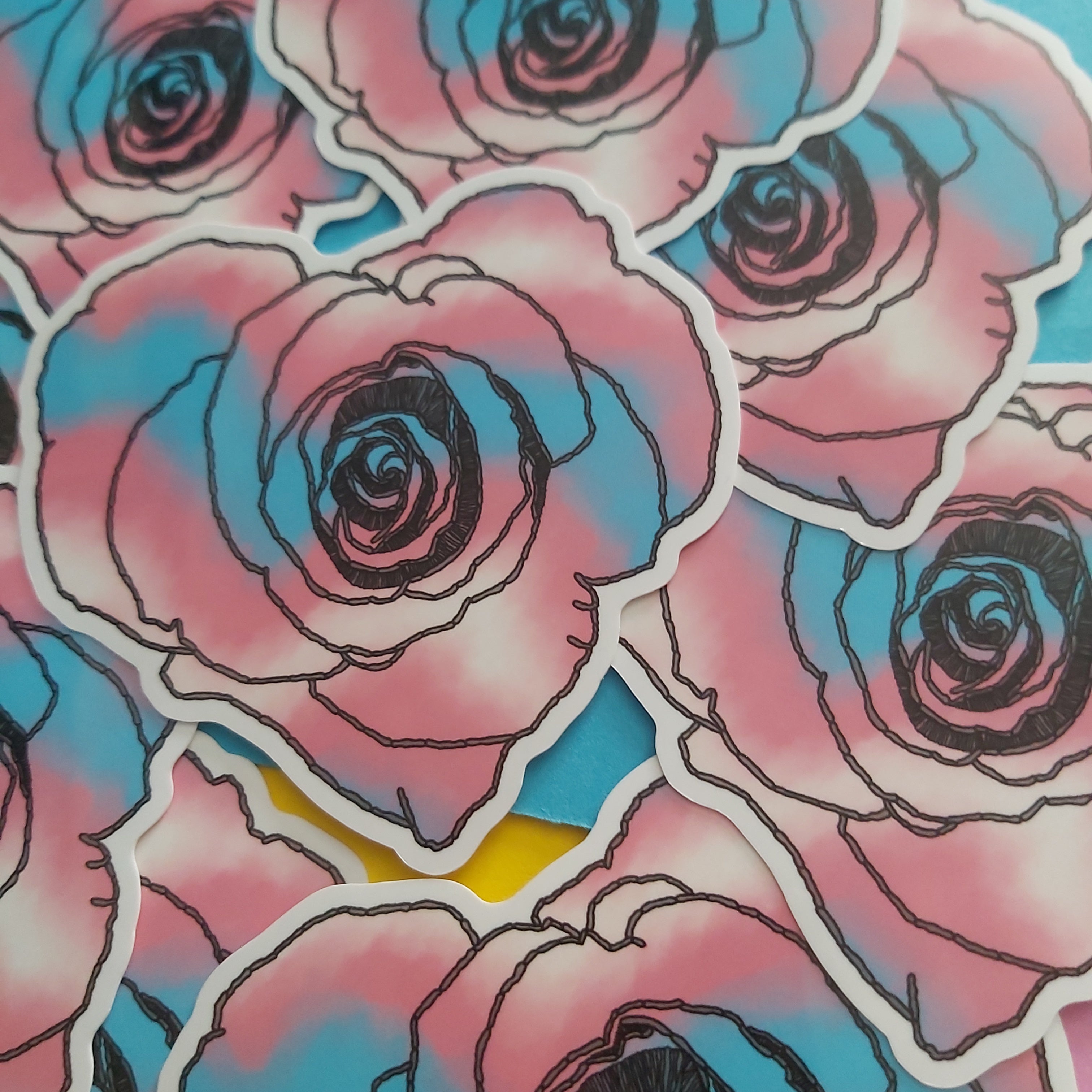 A close-up of multiple die-cut stickers featuring pink and blue watercolor roses with black outlines, layered over a matching pink, blue, and yellow background.