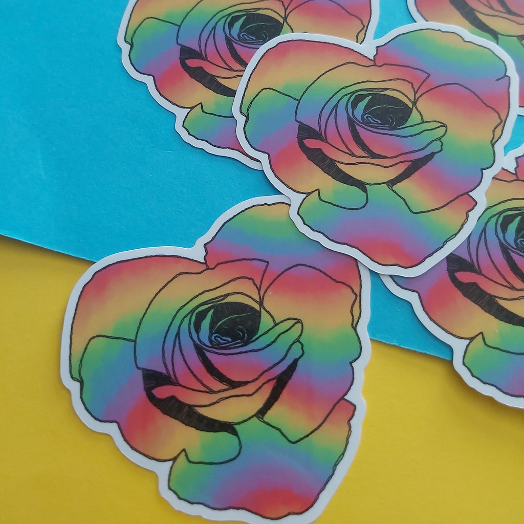 Several die-cut stickers featuring rainbow-gradient roses with black outlines and white borders, arranged on a bright blue and yellow background.