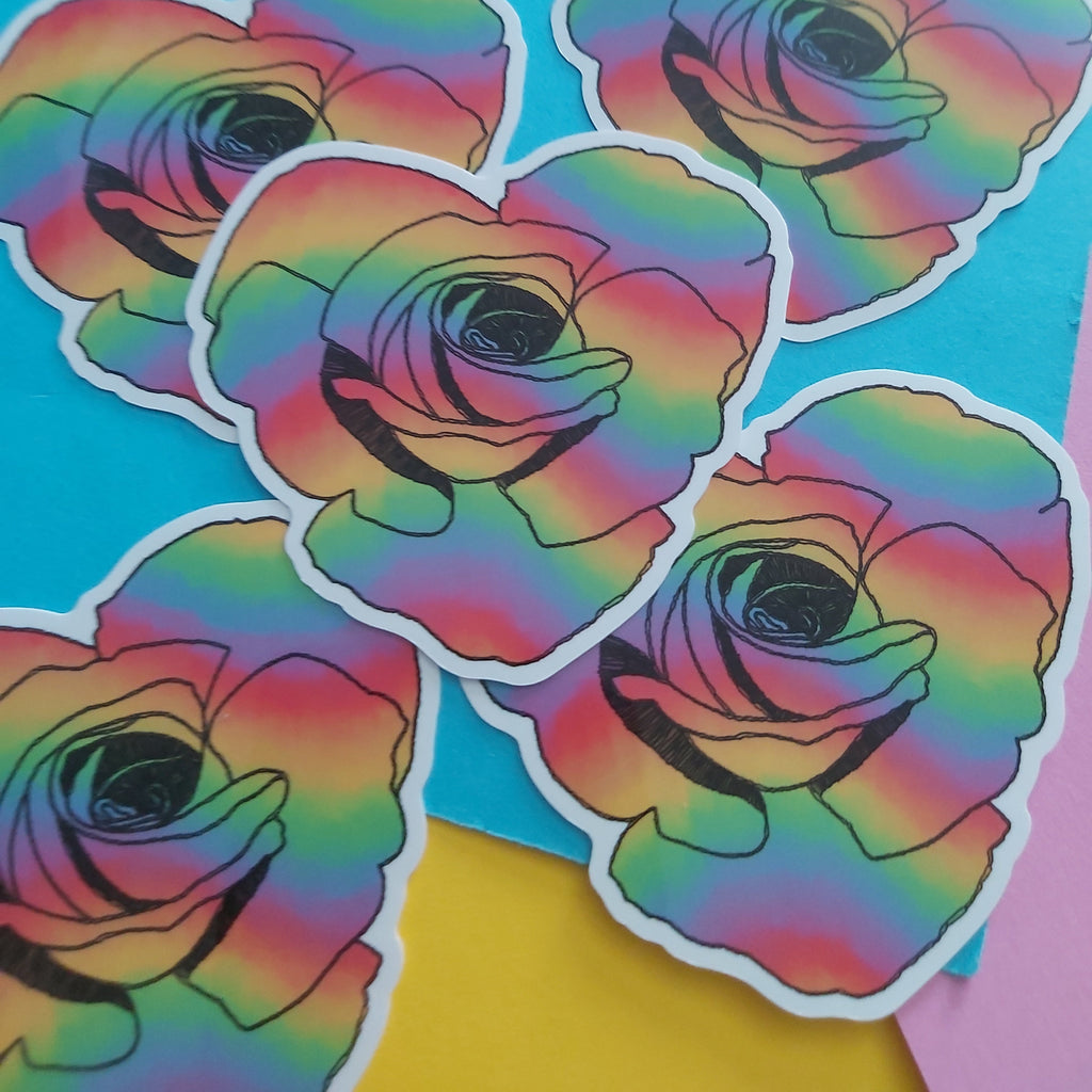 Five die-cut stickers featuring a rainbow-striped rose design with black outlines and white borders, arranged on a bright blue background with yellow and pink paper accents.