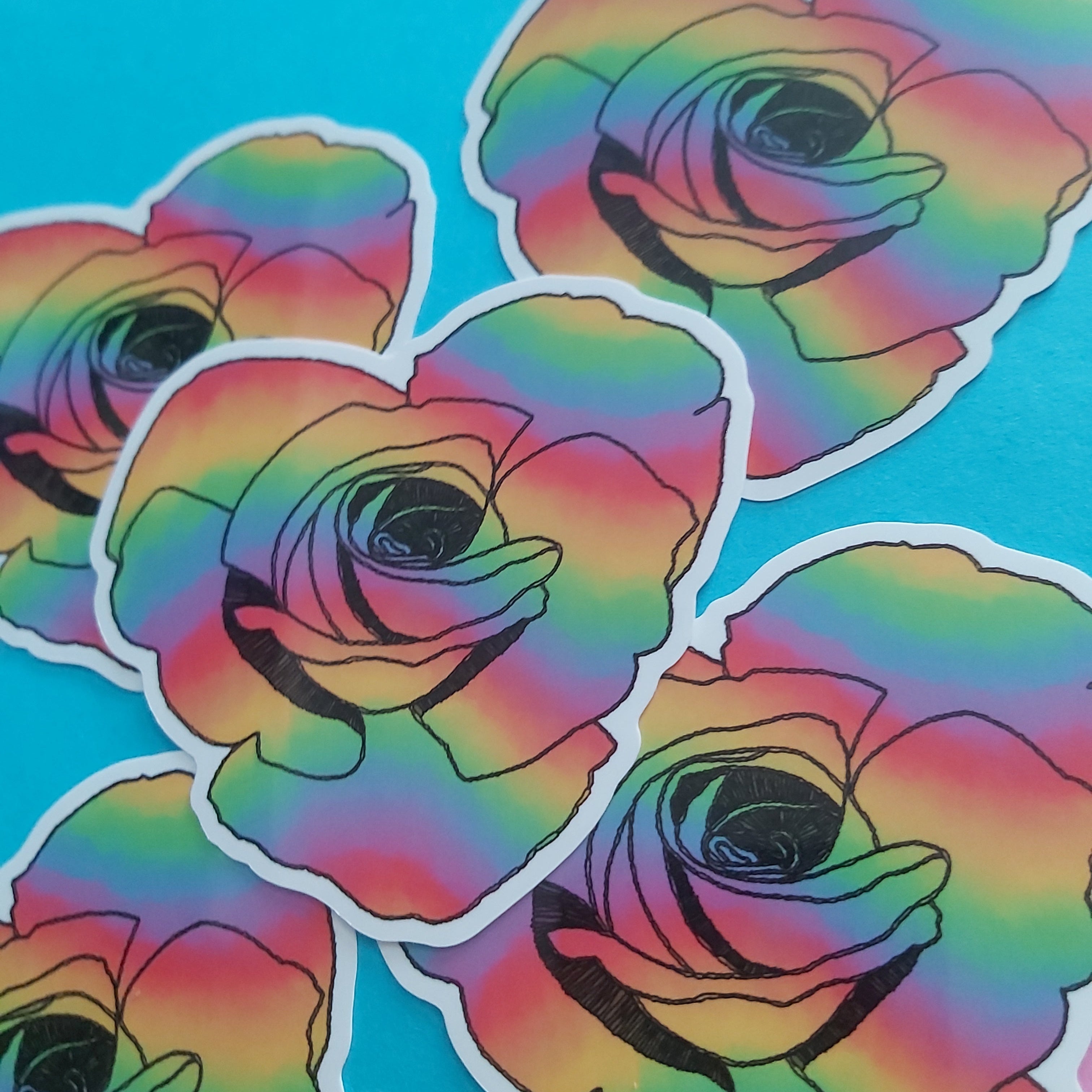 A close-up of several die-cut stickers featuring a stylized rose with a rainbow gradient and black outlines, arranged on a bright blue background with a small yellow area at the bottom.