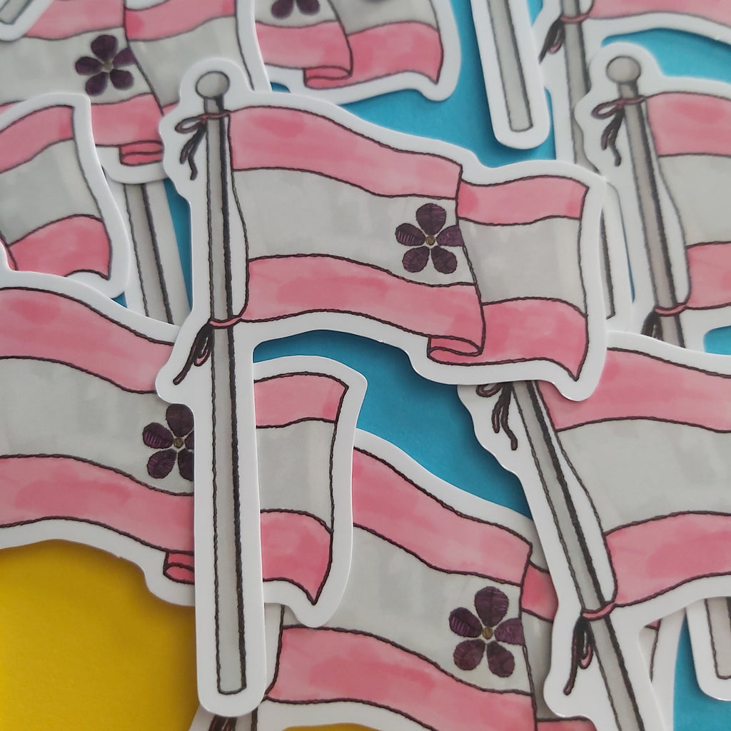 A close-up of multiple die-cut stickers depicting the sapphic pride flag on poles, arranged overlapping on a bright blue and yellow background.