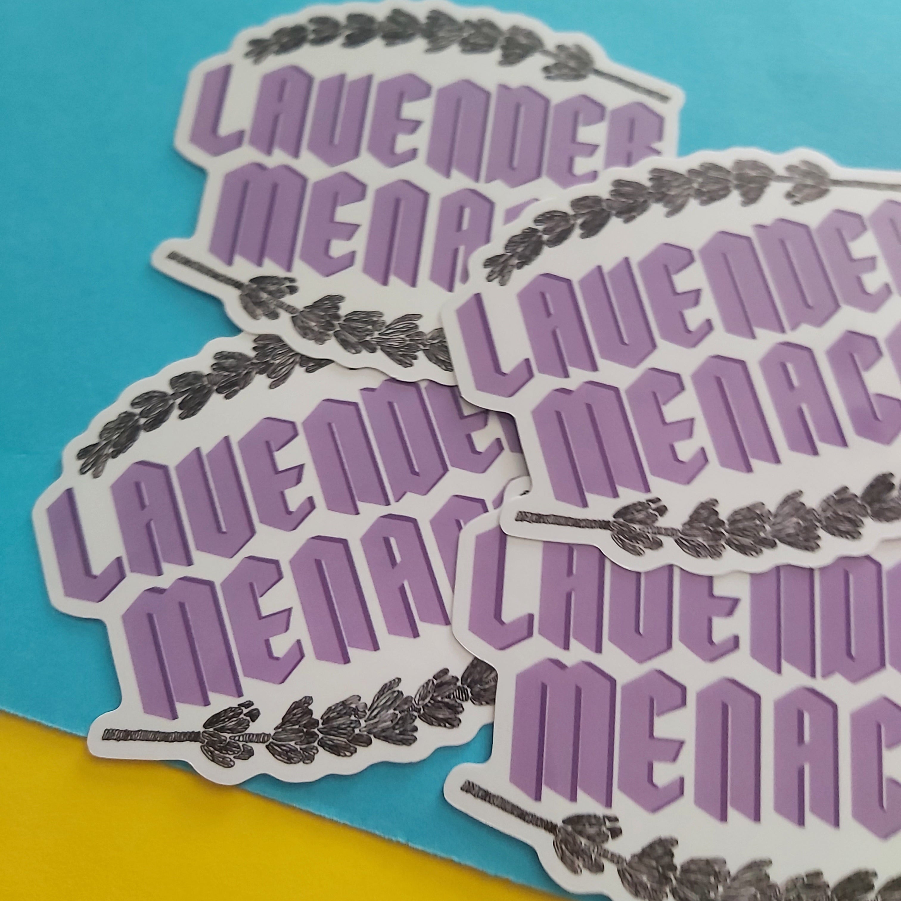 Four die-cut stickers featuring the phrase 'LAVENDER MENACE' in stylised purple lettering with a lavender sprig border, arranged on a split blue and yellow background.