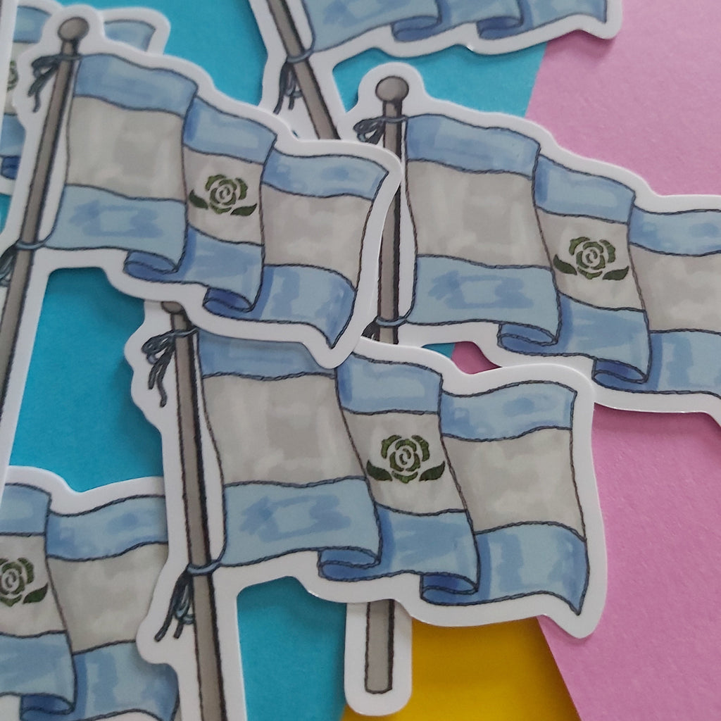 A close-up of several die-cut stickers depicting the Achillean flag on poles, arranged on a colorful background with cyan, pink, and yellow paper.